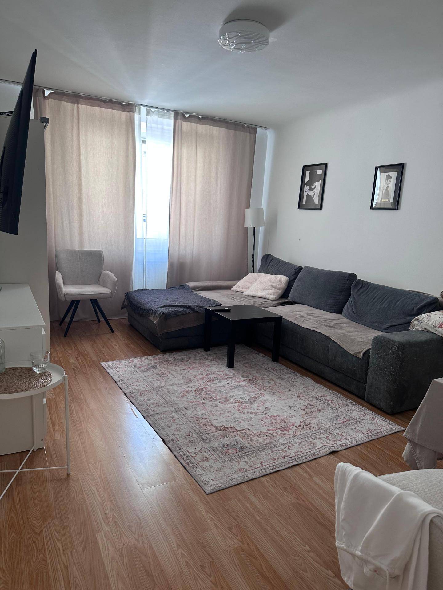 Wohnzimmer mit großem Ecksofa, Holzboden und hellem Fensterbereich.
