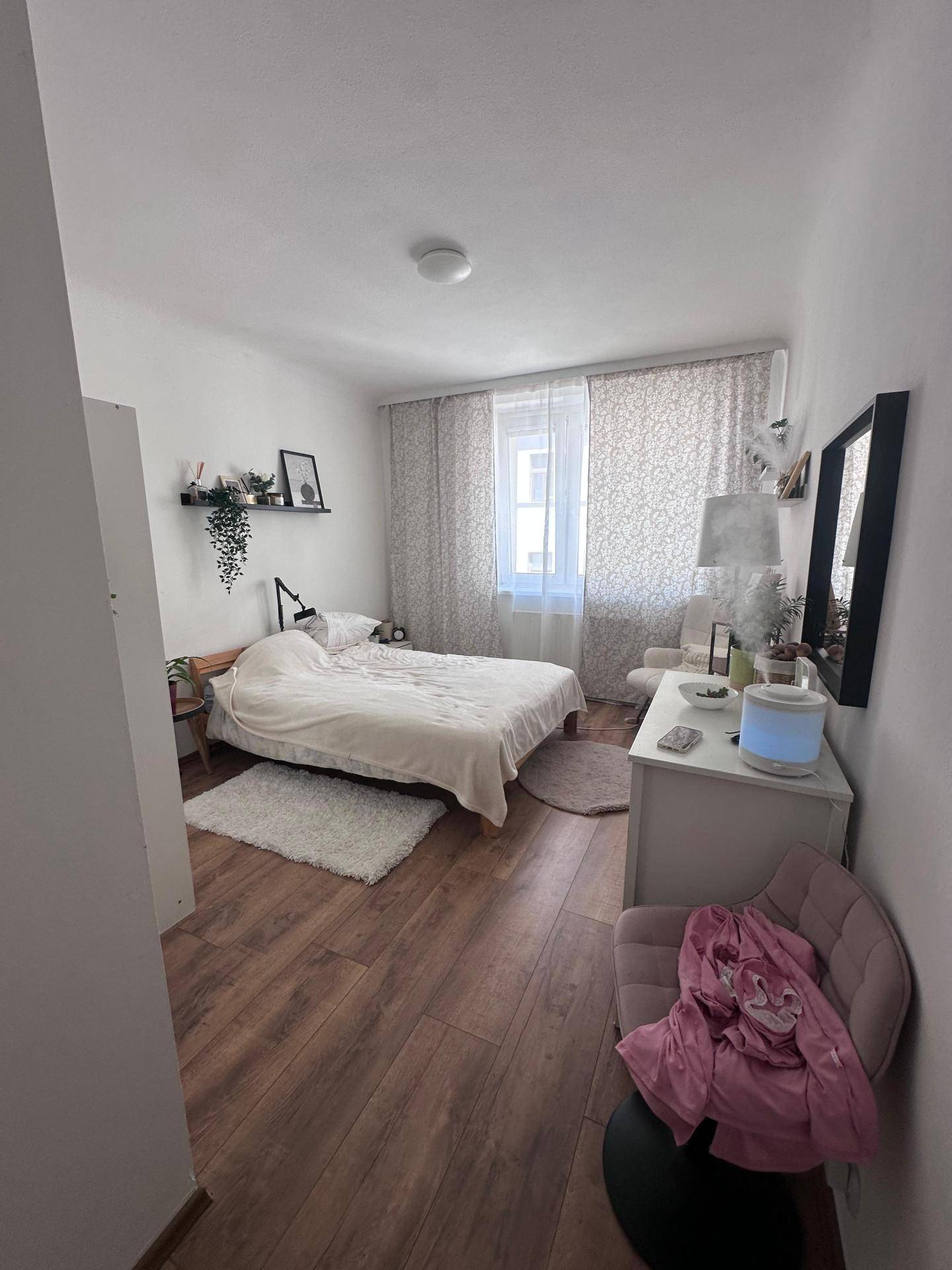 Gemütliches Schlafzimmer mit Holzboden, großem Bett und Fenster mit Vorhängen.