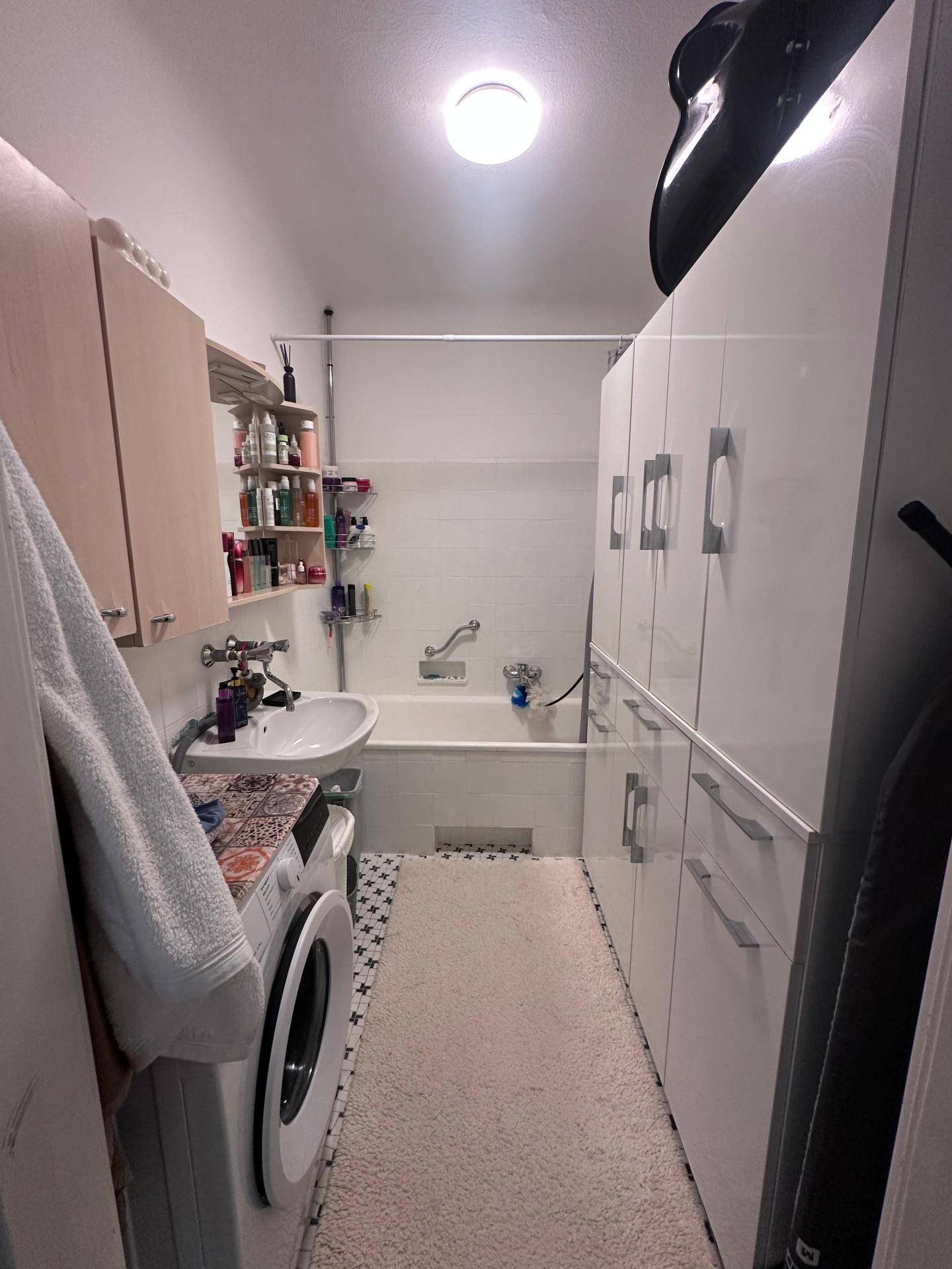 Schlichtes Badezimmer mit Badewanne, Waschbecken und Waschmaschine.