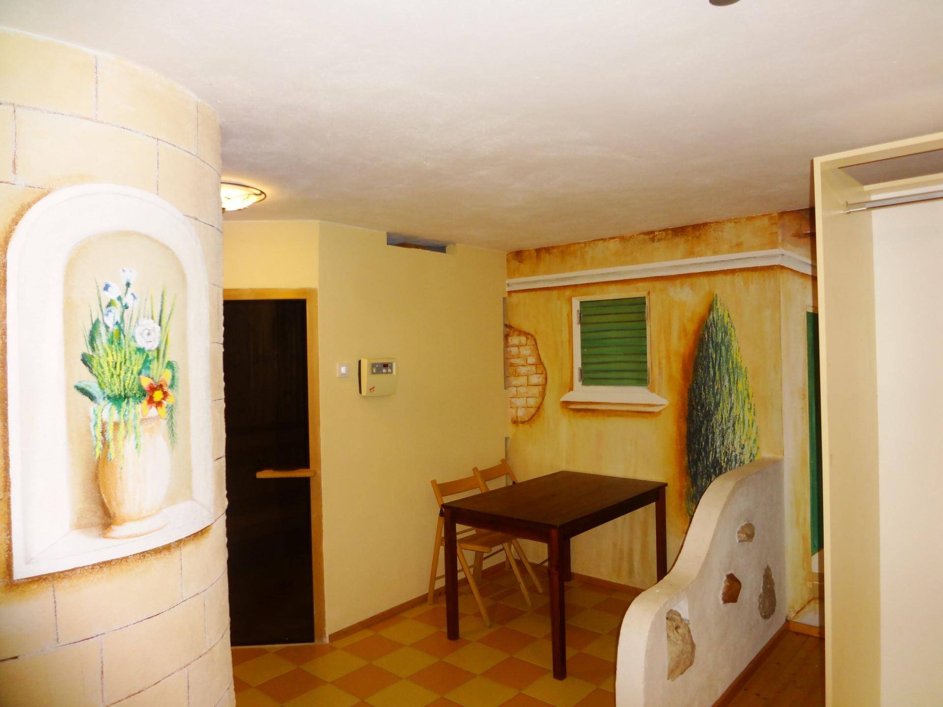 Essbereich mit rustikaler Wandmalerei, Holztisch und Stühlen, sowie gefliestem Boden.