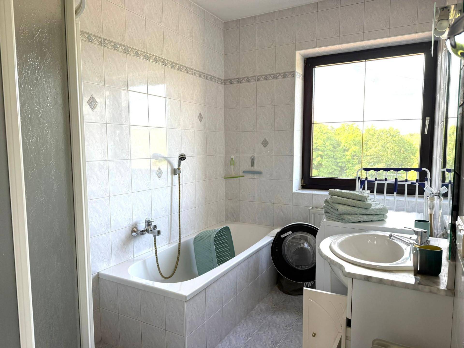 Gefliestes Badezimmer mit Badewanne, Dusche, Waschbecken und einem Fenster mit Ausblick.