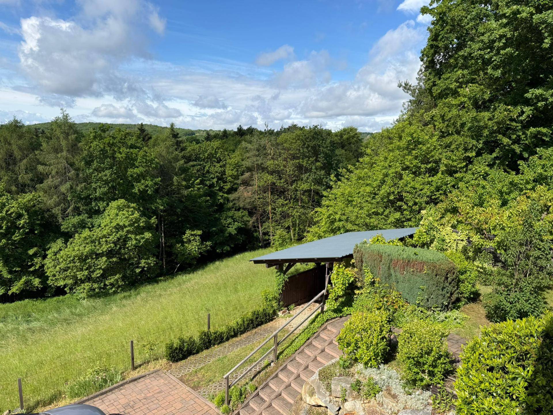 Garten mit überdachtem Bereich und weitem Blick über die umliegende Natur und Hügellandschaft.