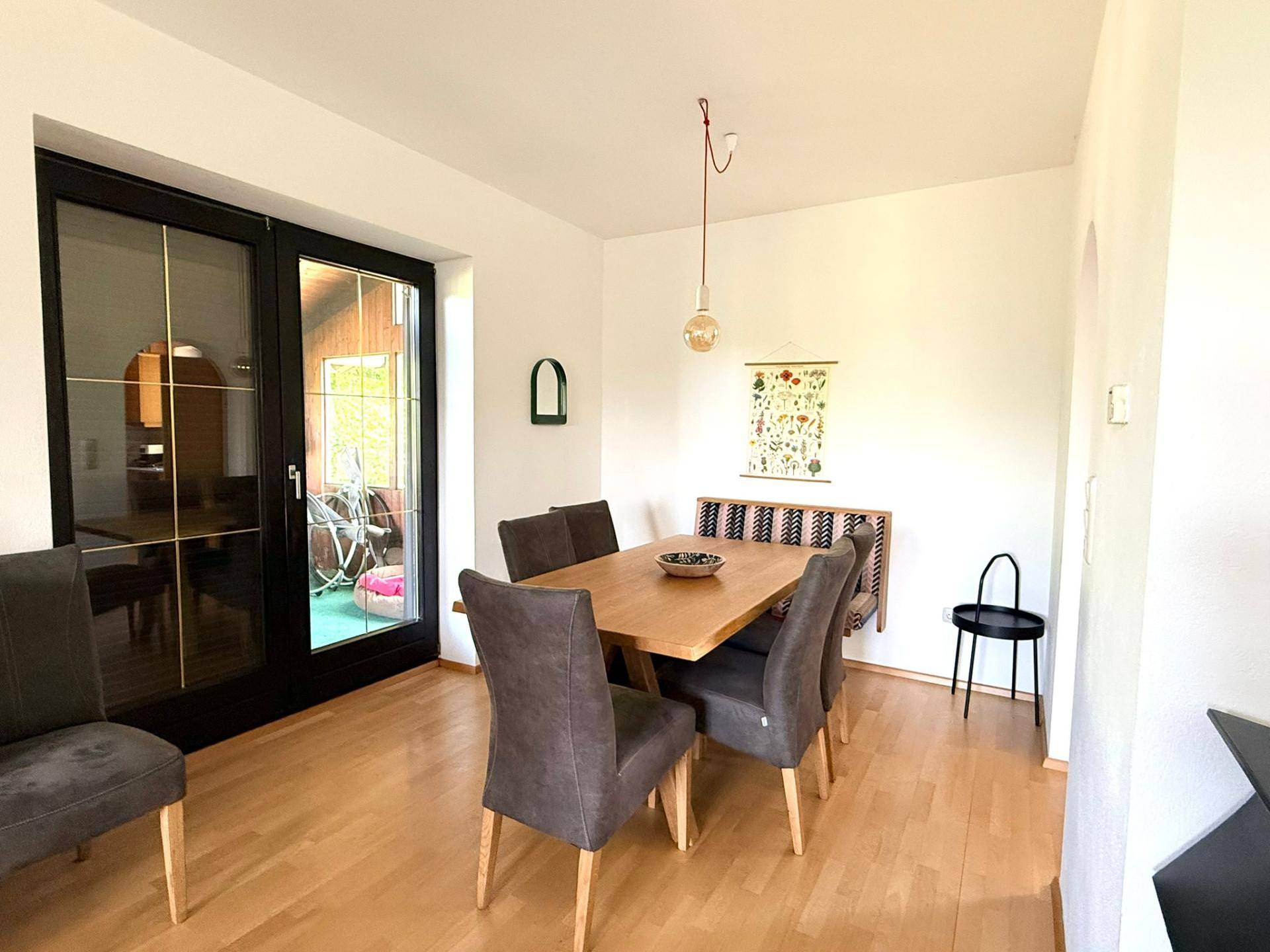 Essbereich mit Holztisch, modernen Stühlen und Zugang zu einem Außenbereich durch eine Glastür.