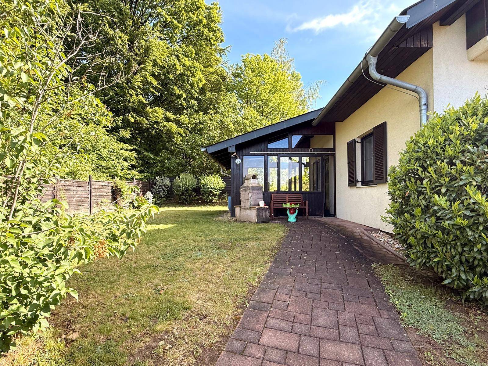 Seitlicher Gartenbereich mit Rasenfläche, gepflastertem Weg und einem Wintergarten.