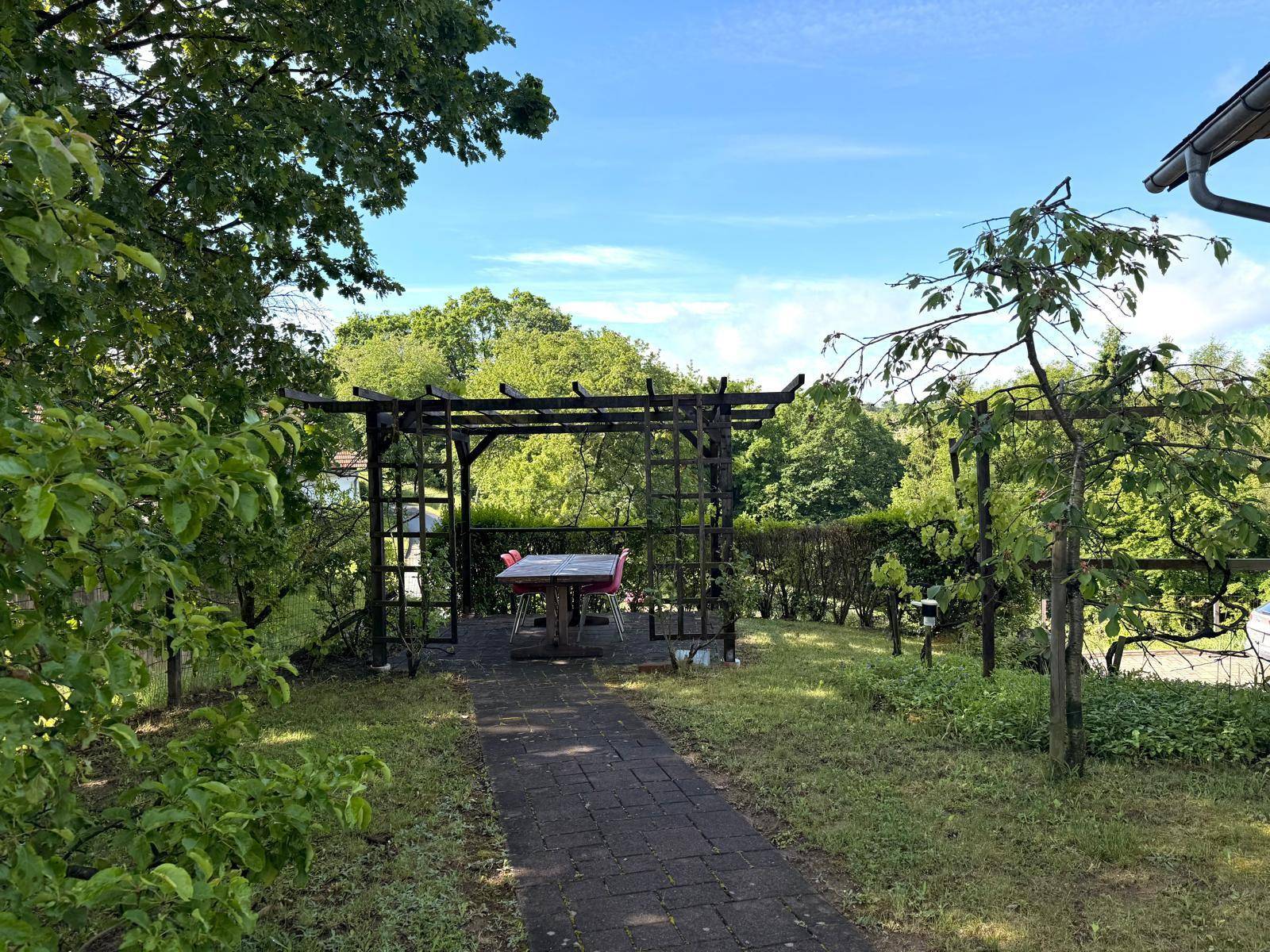 Gartenbereich mit einer Holzpergola, Sitzgelegenheit und einem gepflasterten Weg.