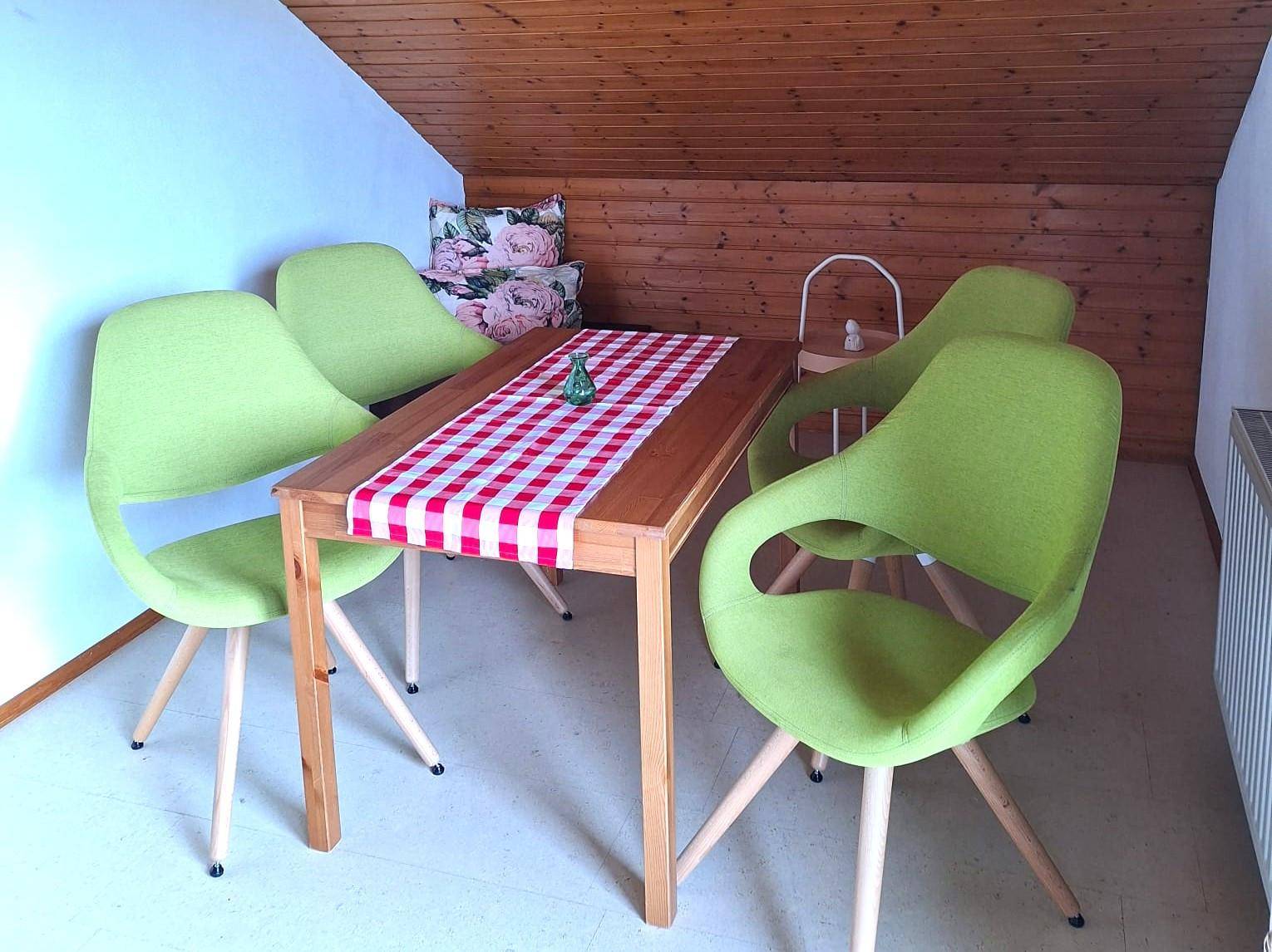 Essbereich im Dachgeschoss mit Holztäfelung, modernem Tisch und farbenfrohen Stühlen.