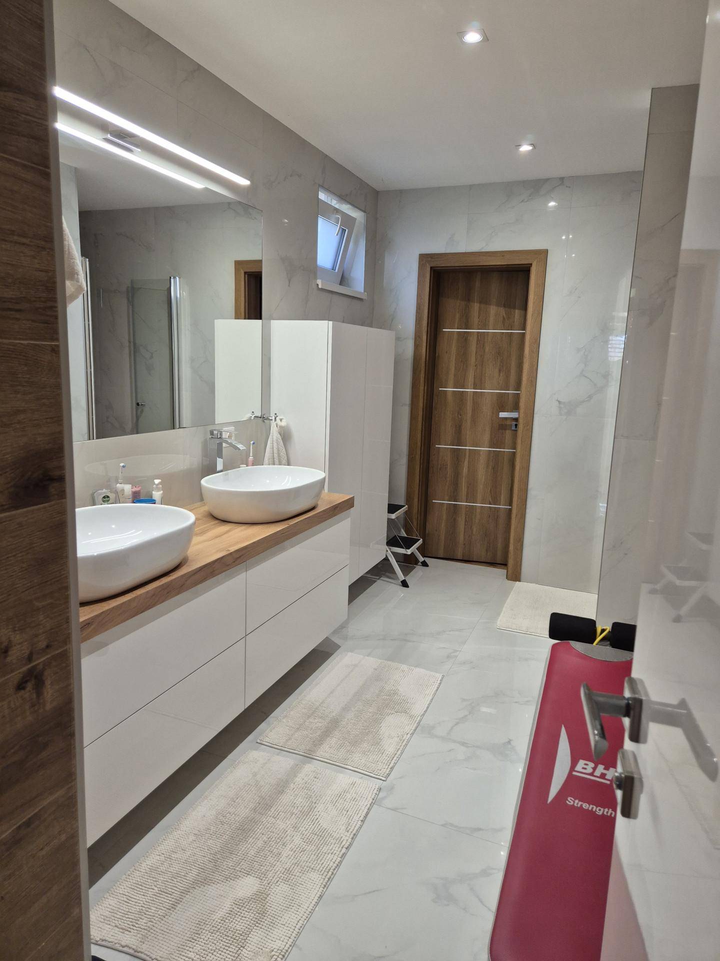 Modernes Badezimmer mit Doppelwaschbecken, Holzelementen und großformatigen Fliesen.