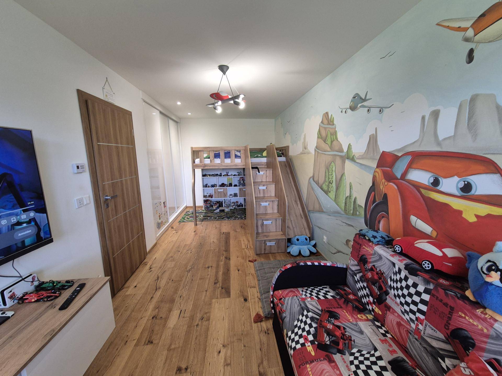Kinderzimmer mit farbenfroher Wandmalerei, Hochbett und Holzboden.