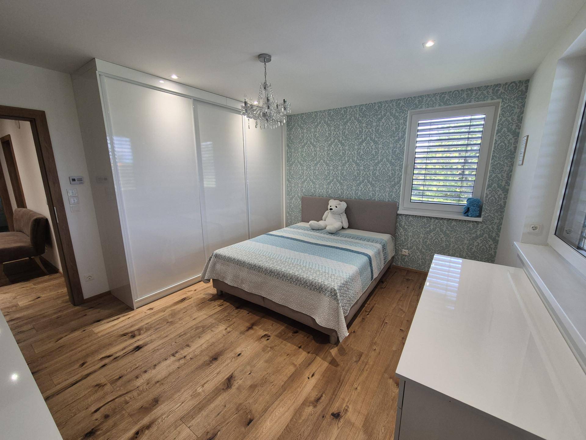 Gemütliches Schlafzimmer mit Doppelbett, gemusterter Tapete und weißem Kleiderschrank.