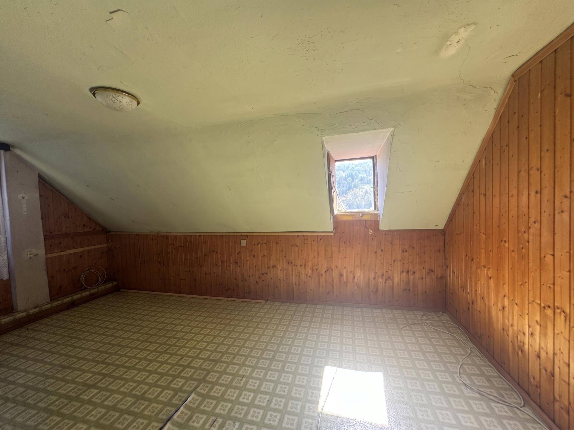 Geräumiger Dachgeschossraum mit Holzverkleidung und einem kleinen Fenster mit Blick ins Grüne.