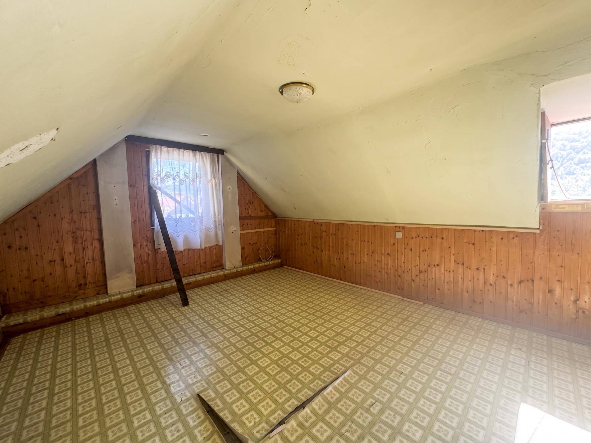 Dachgeschossraum mit Holzvertäfelung, schrägen Wänden und gemustertem Bodenbelag.