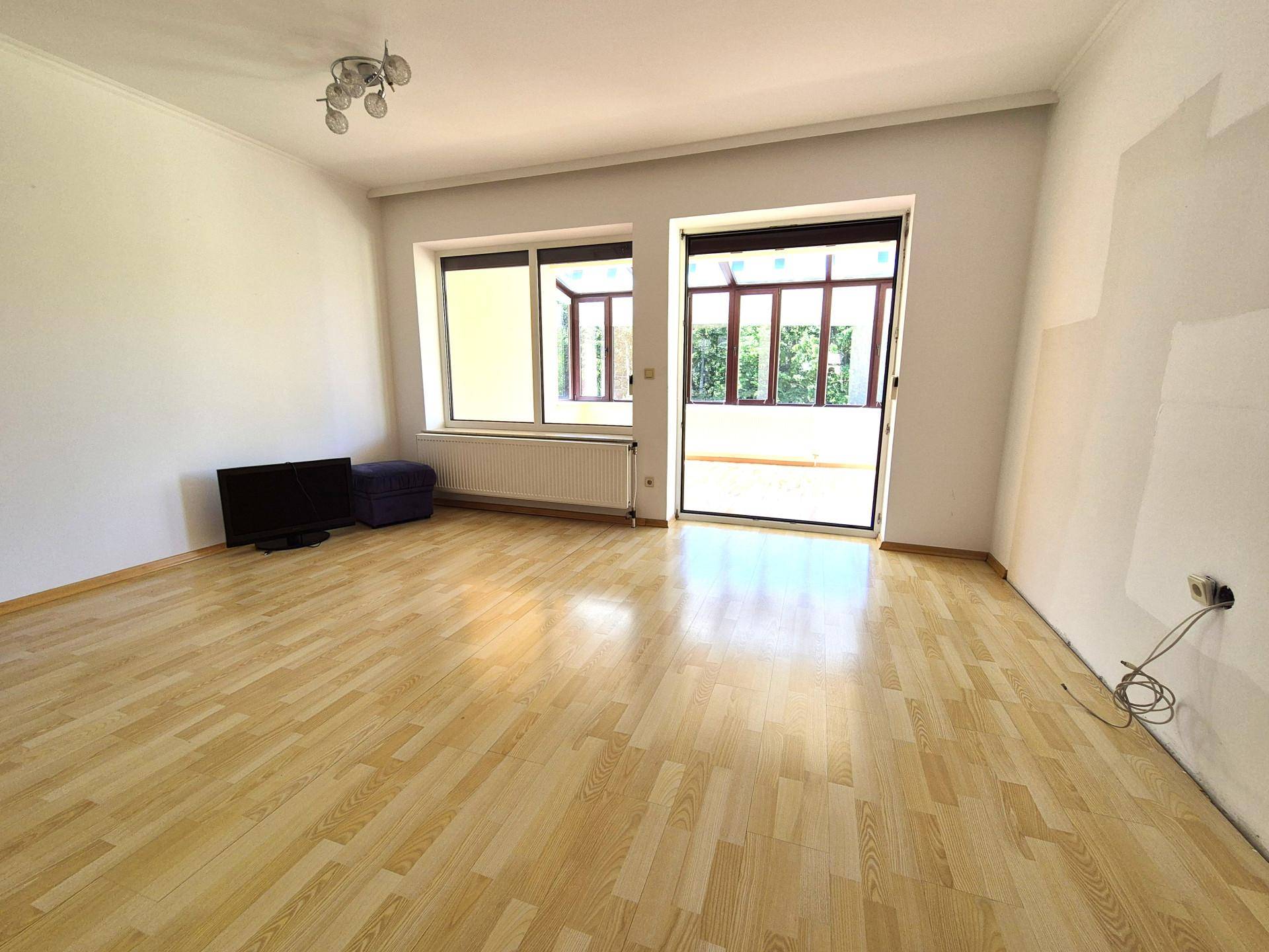 Geräumiges Wohnzimmer mit Laminatboden und Zugang zu einem hellen Wintergarten.