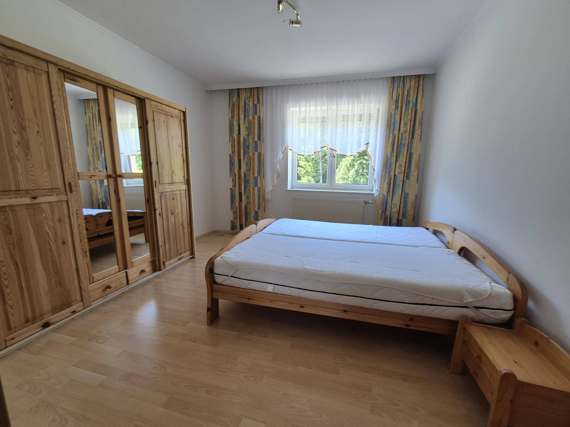 Schlafzimmer mit Holzbett, großem Holzschrank und Blick in den Garten.