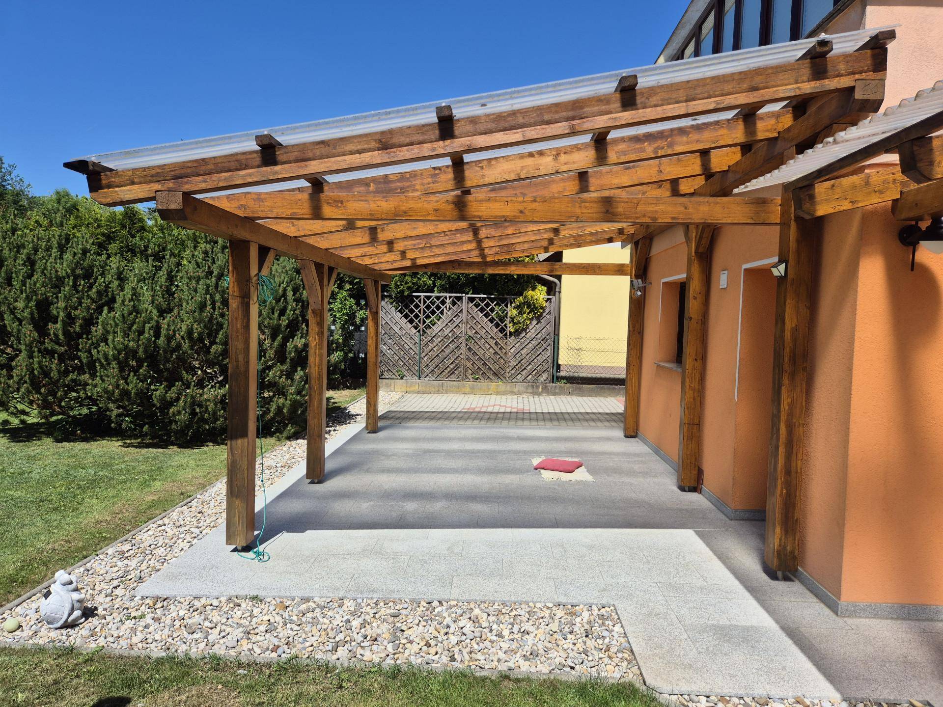 Überdachte Terrasse mit Holzpergola und Kiesbereich, ideal für entspannte Stunden im Freien.