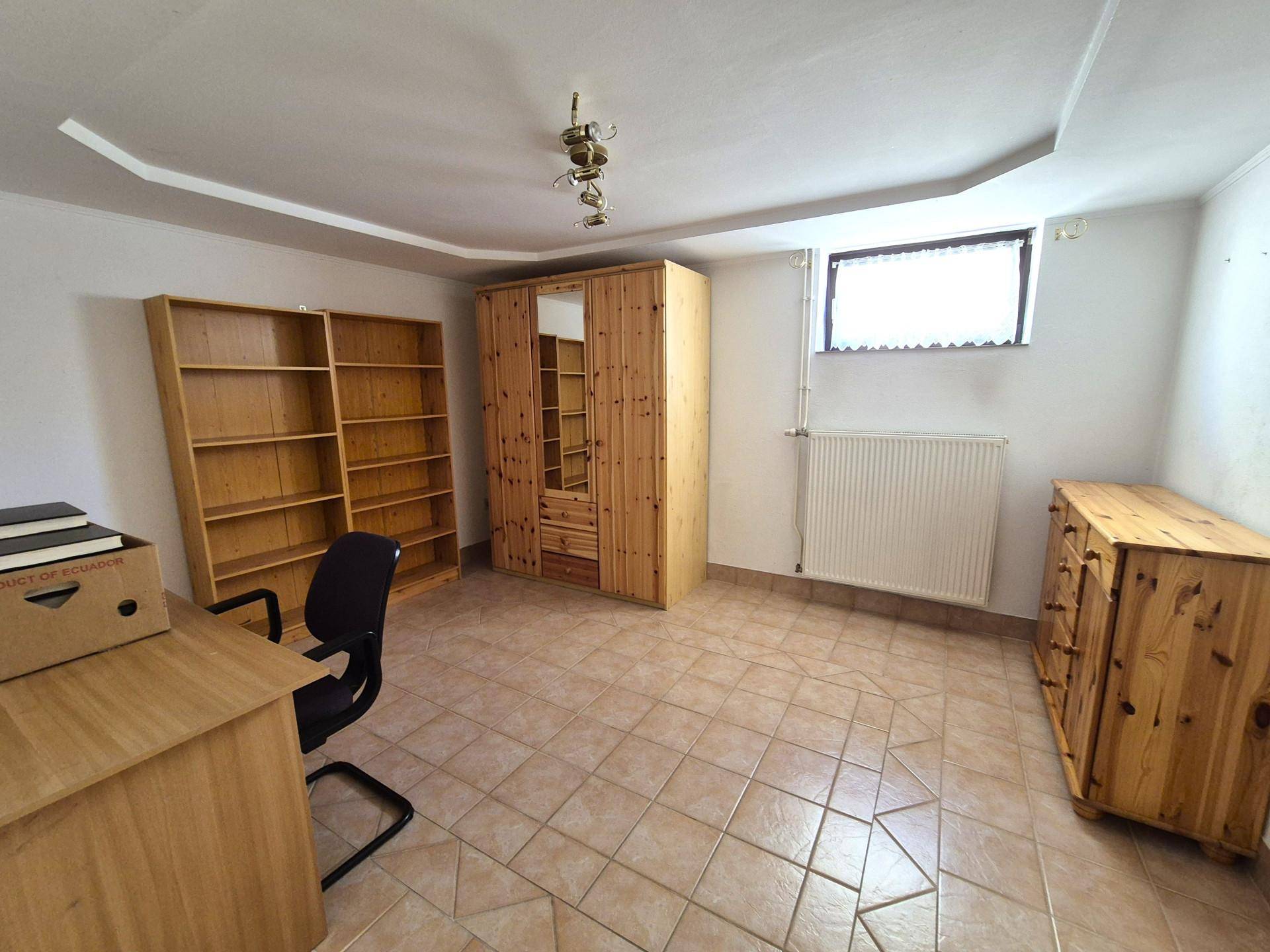 Helles Arbeitszimmer mit Fliesenboden, Holzregalen und einem großen Schreibtisch.