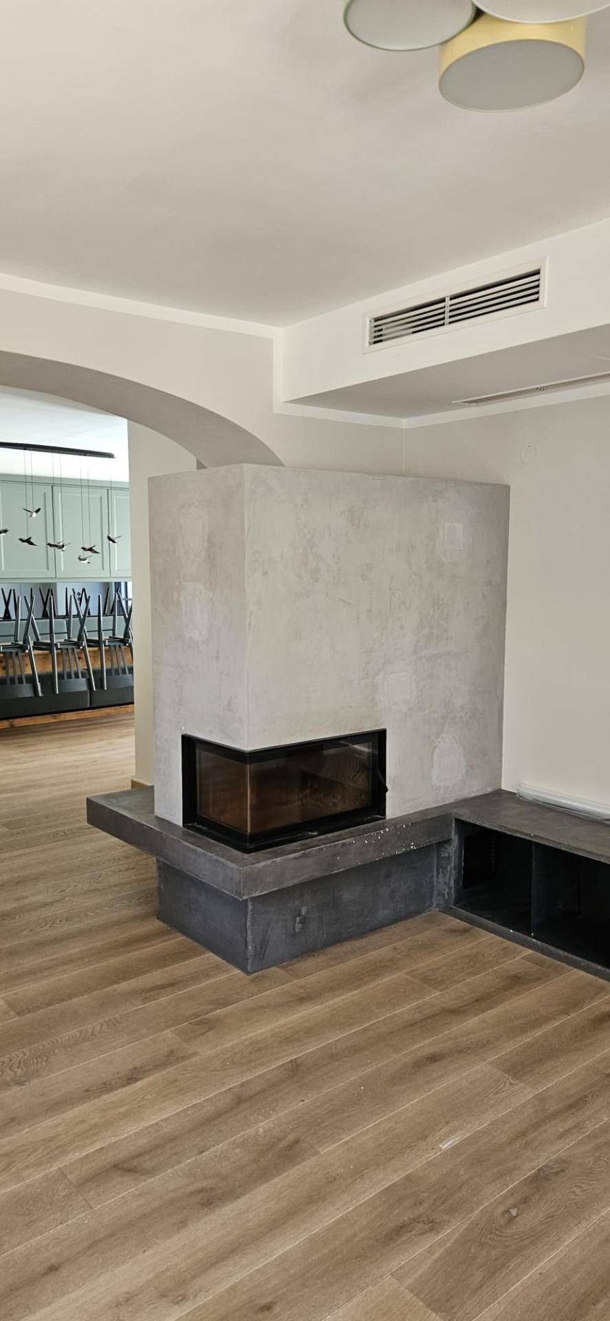 Heller Wohnbereich mit modernem Kamin und Holzboden, offen zu einem weiteren Raum.