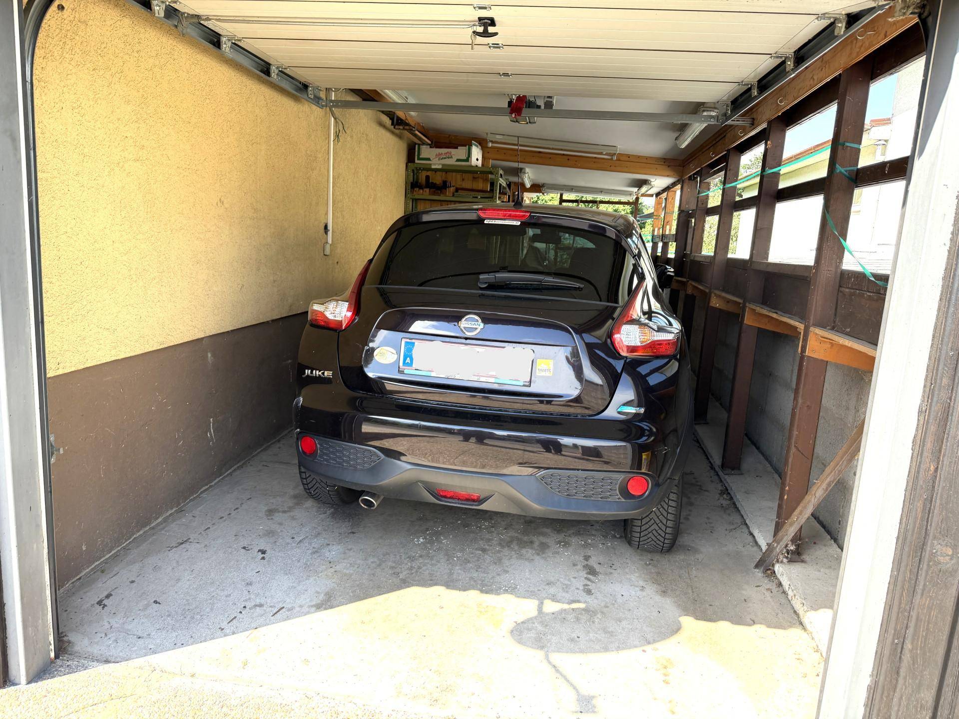 Einzelgarage mit einem geparkten Auto und direktem Zugang zum Haus.