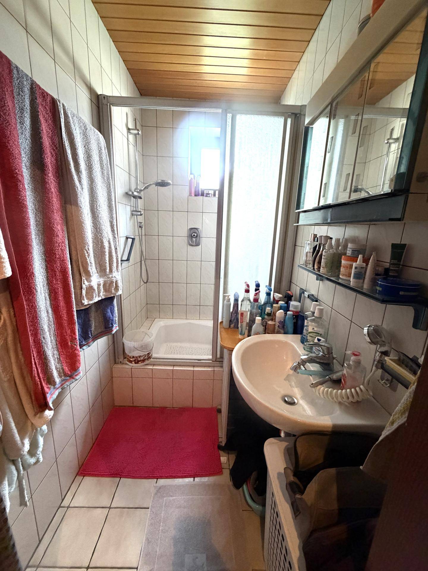 Kleines Badezimmer mit Duschkabine, Waschbecken und Fliesen an Wänden und Boden.