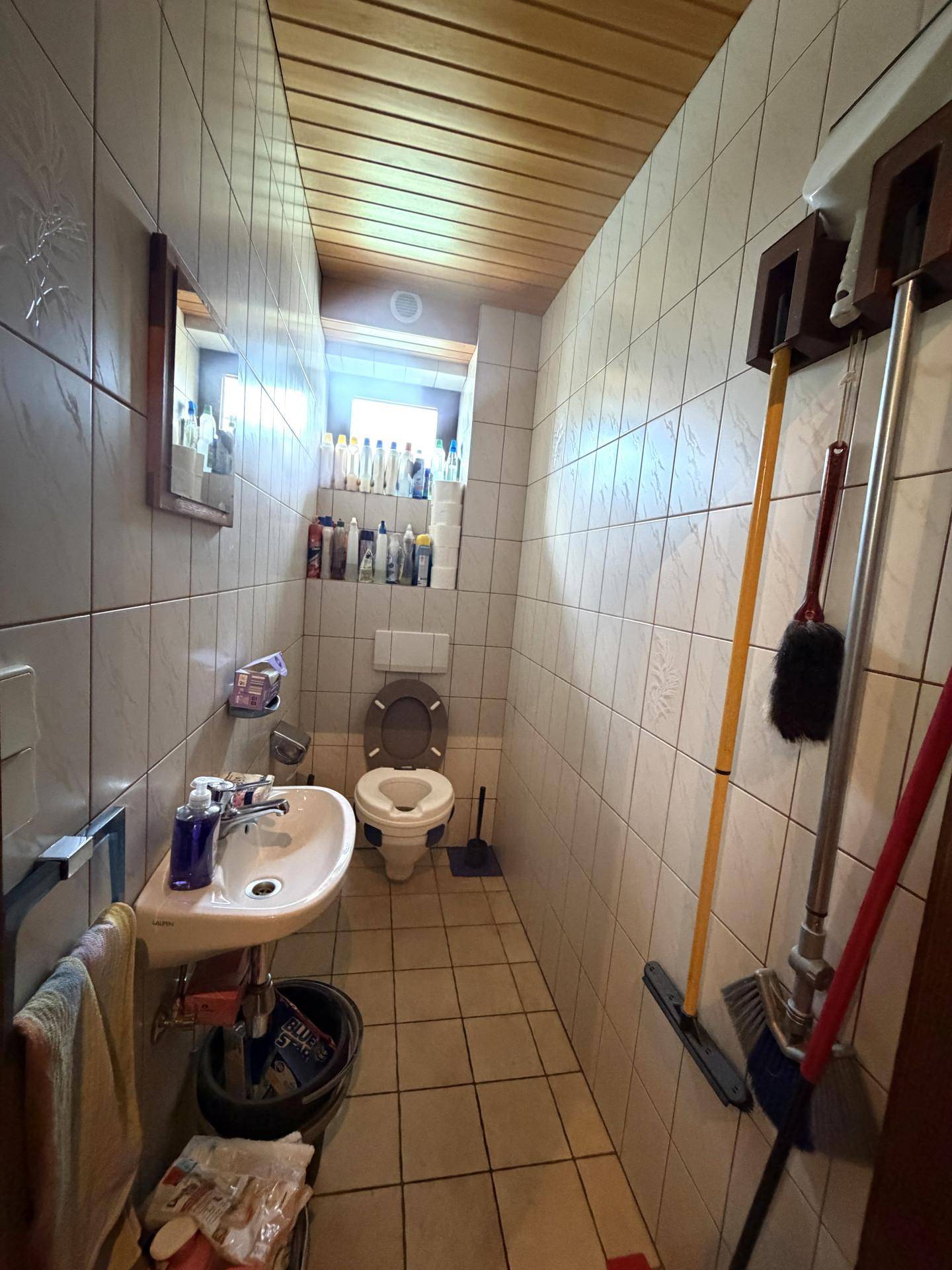 Schmale Gästetoilette mit WC, kleinem Waschbecken und hellen Fliesen.