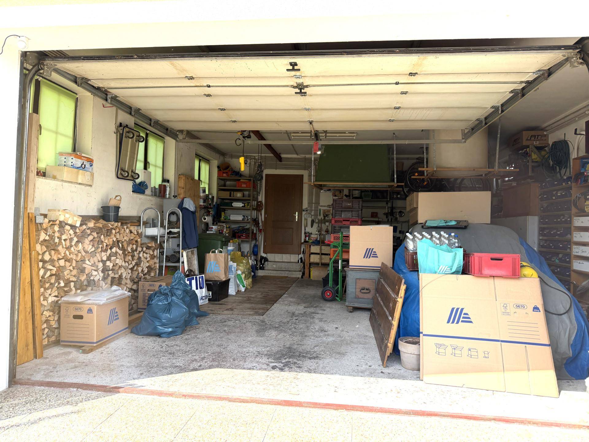 Geräumige Garage mit viel Stauraum, Holzstapeln und Tageslicht durch Fenster.