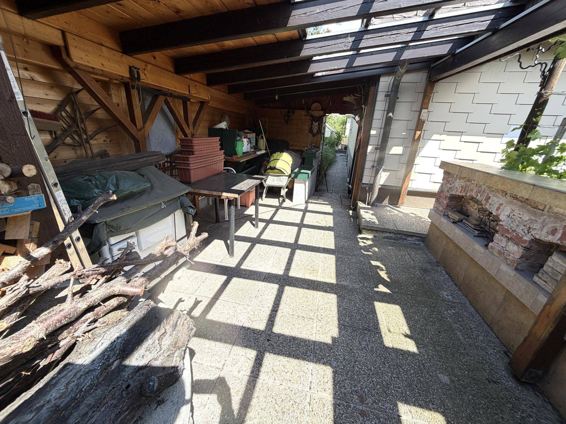 Überdachte Terrasse mit Holzbalken und gemauertem Grillbereich.