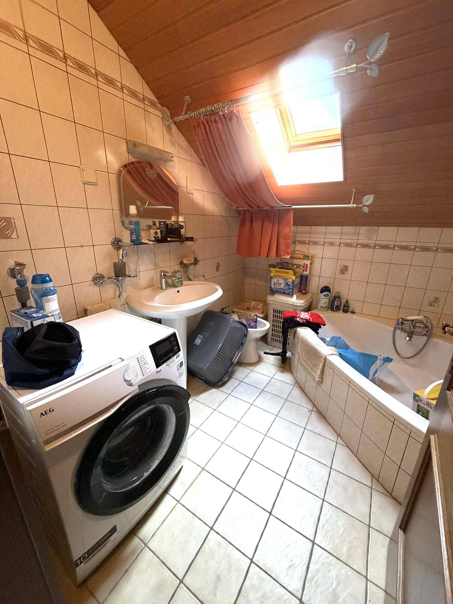 Badezimmer im Dachgeschoss mit Badewanne, Waschmaschine und Dachfenster.