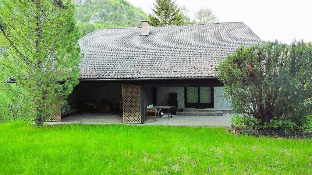 Rückseite des Hauses mit überdachter Terrasse und großem, grünem Gartenbereich.