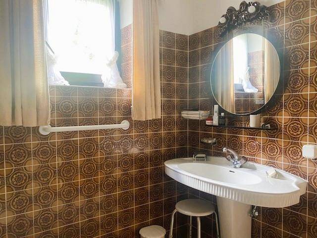 Badezimmer mit braunen Fliesen, Fenster und einem einzelnen Waschbecken mit Spiegel.