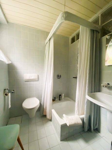 Badezimmer mit hellblauen Fliesen, Toilette und einer Duschwanne mit Vorhang.