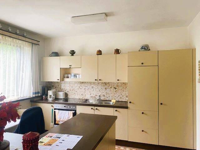 Funktionale Küche mit beigefarbenen Schränken, Fliesenrückwand und Essbereich am Fenster.