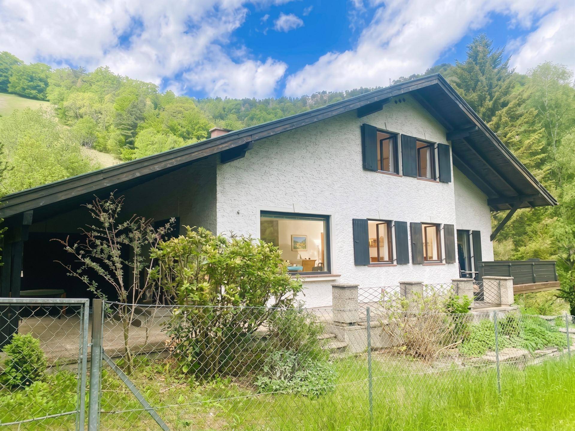 Seitenansicht des Hauses mit überdachtem Bereich und Blick auf die umliegende grüne Natur.