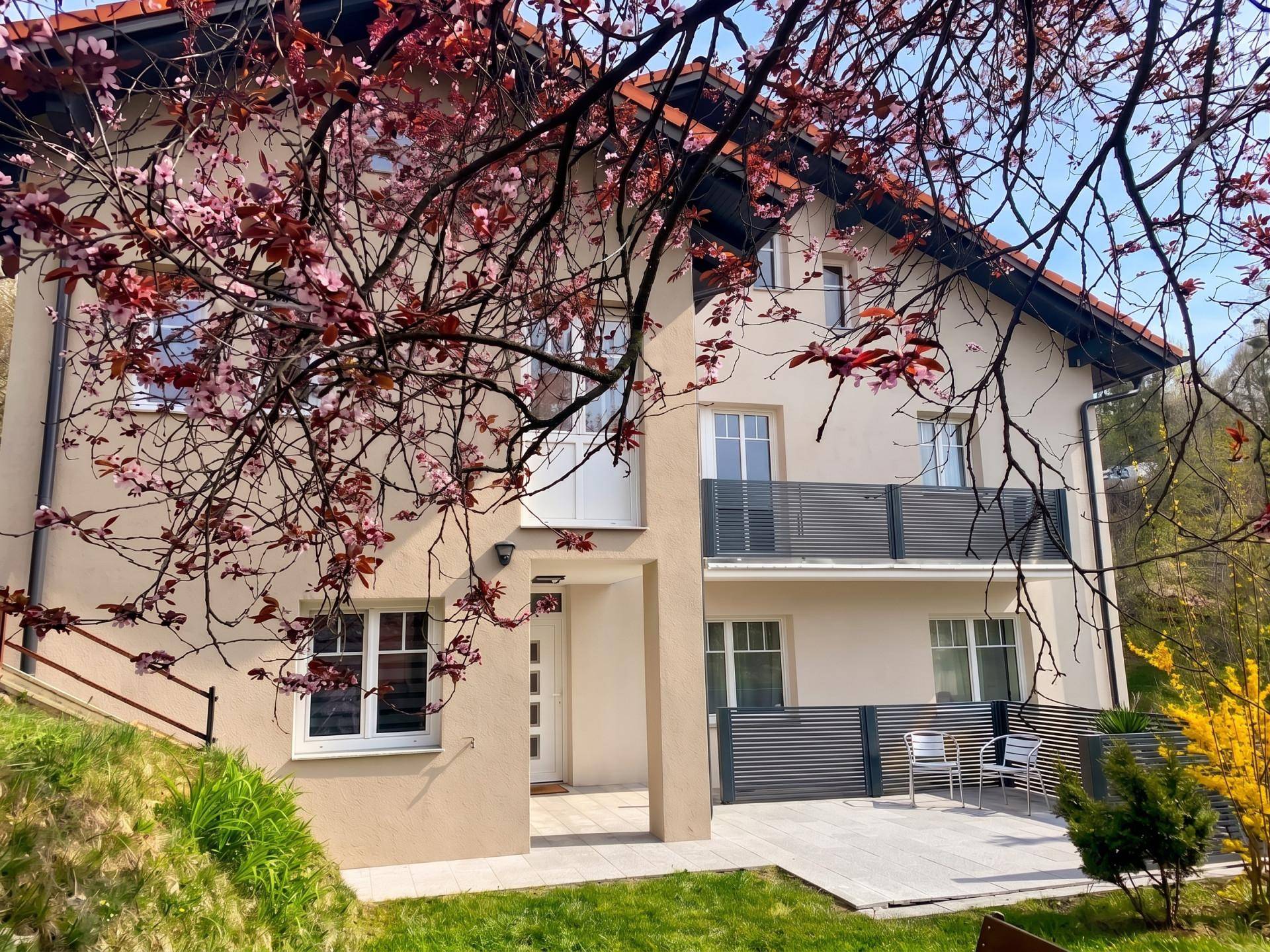 Modernes Haus mit heller Fassade, Balkonen und einer kleinen gepflasterten Terrasse im Frühling.