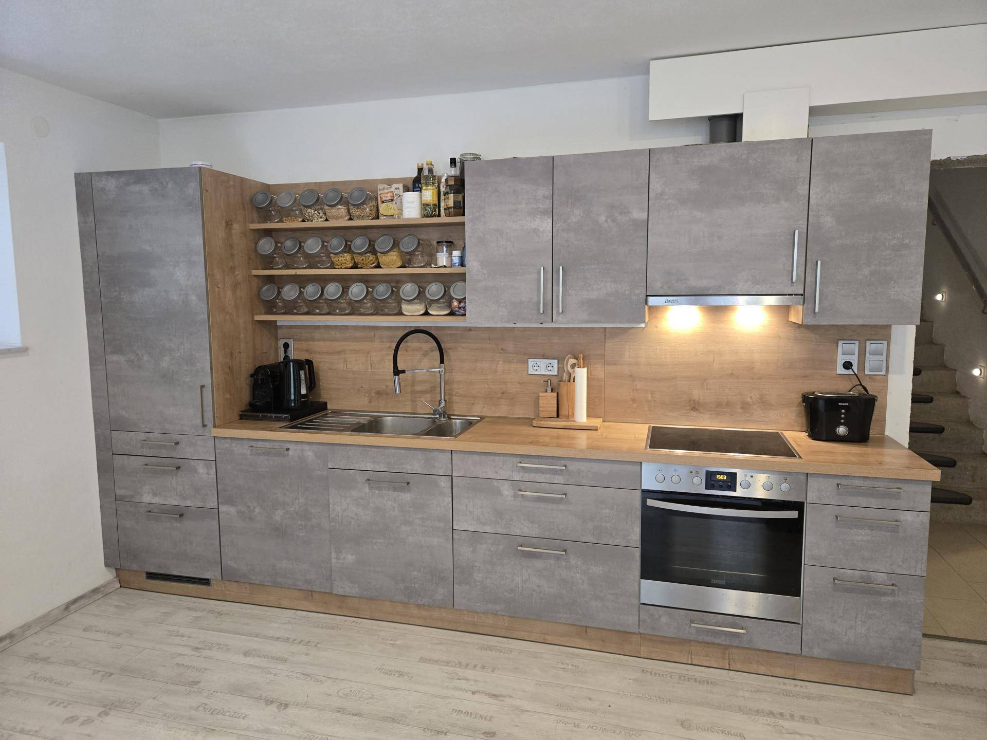 Moderne Einbauküche in Grau und Holzoptik mit Induktionskochfeld und viel Stauraum für Gewürze.