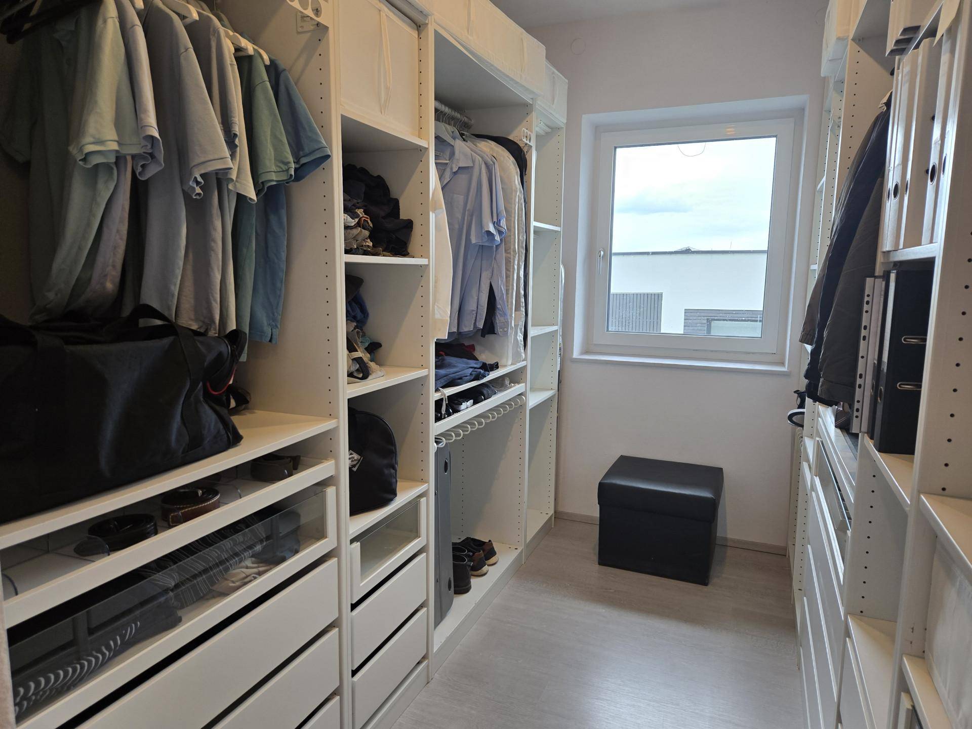 Geräumiger begehbarer Kleiderschrank mit viel Stauraum, Regalen und einem Fenster für Tageslicht.
