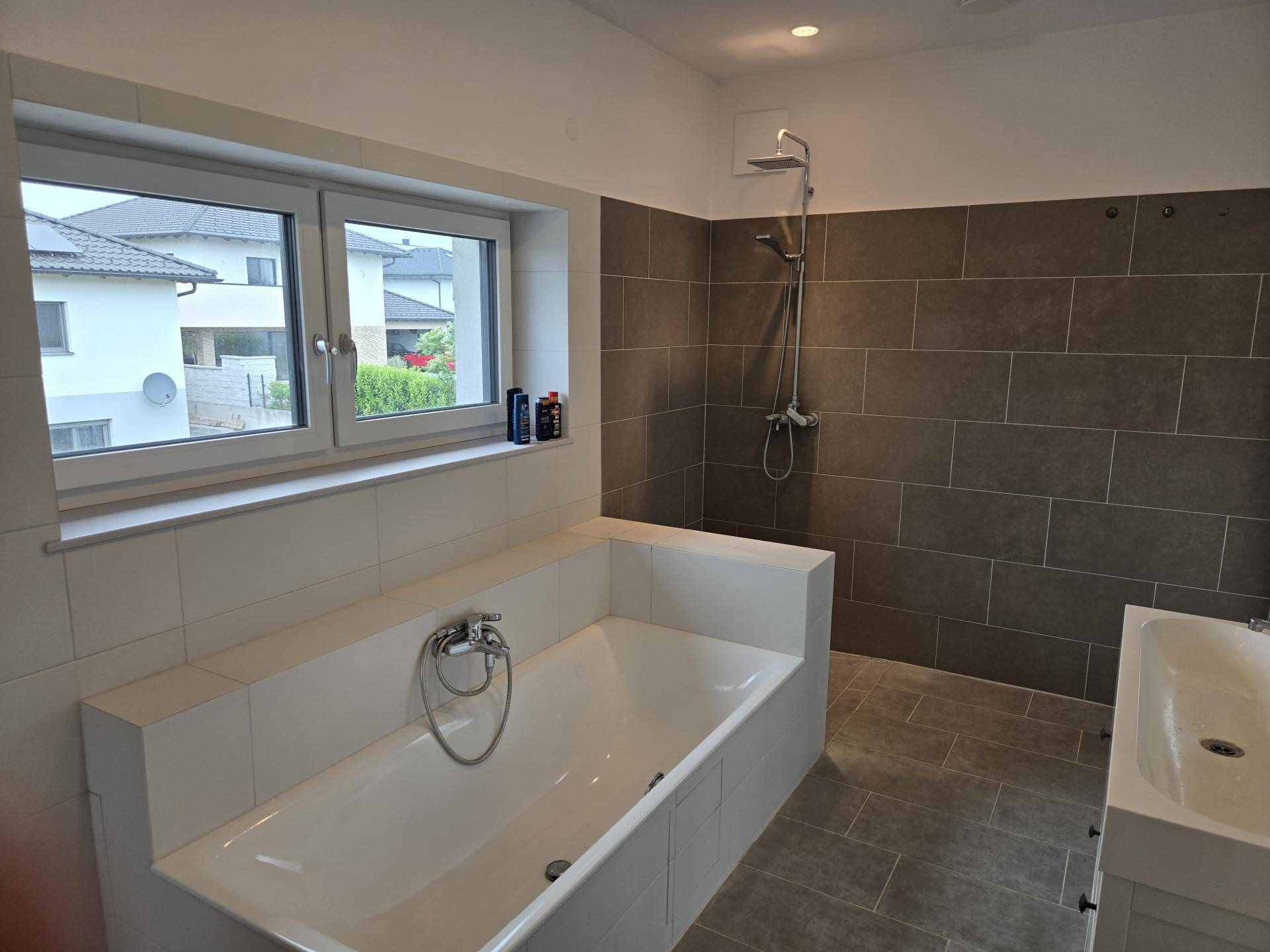 Modernes Badezimmer mit Badewanne, Dusche und großformatigen Fliesen in Grau und Weiß.