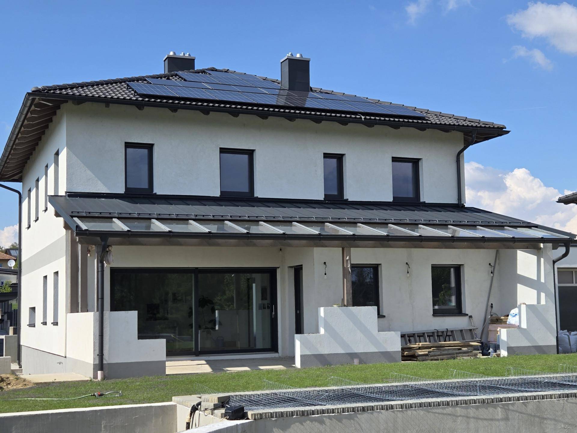 Rückansicht des modernen Einfamilienhauses mit Photovoltaikanlage auf dem Dach und Gartenbereich.