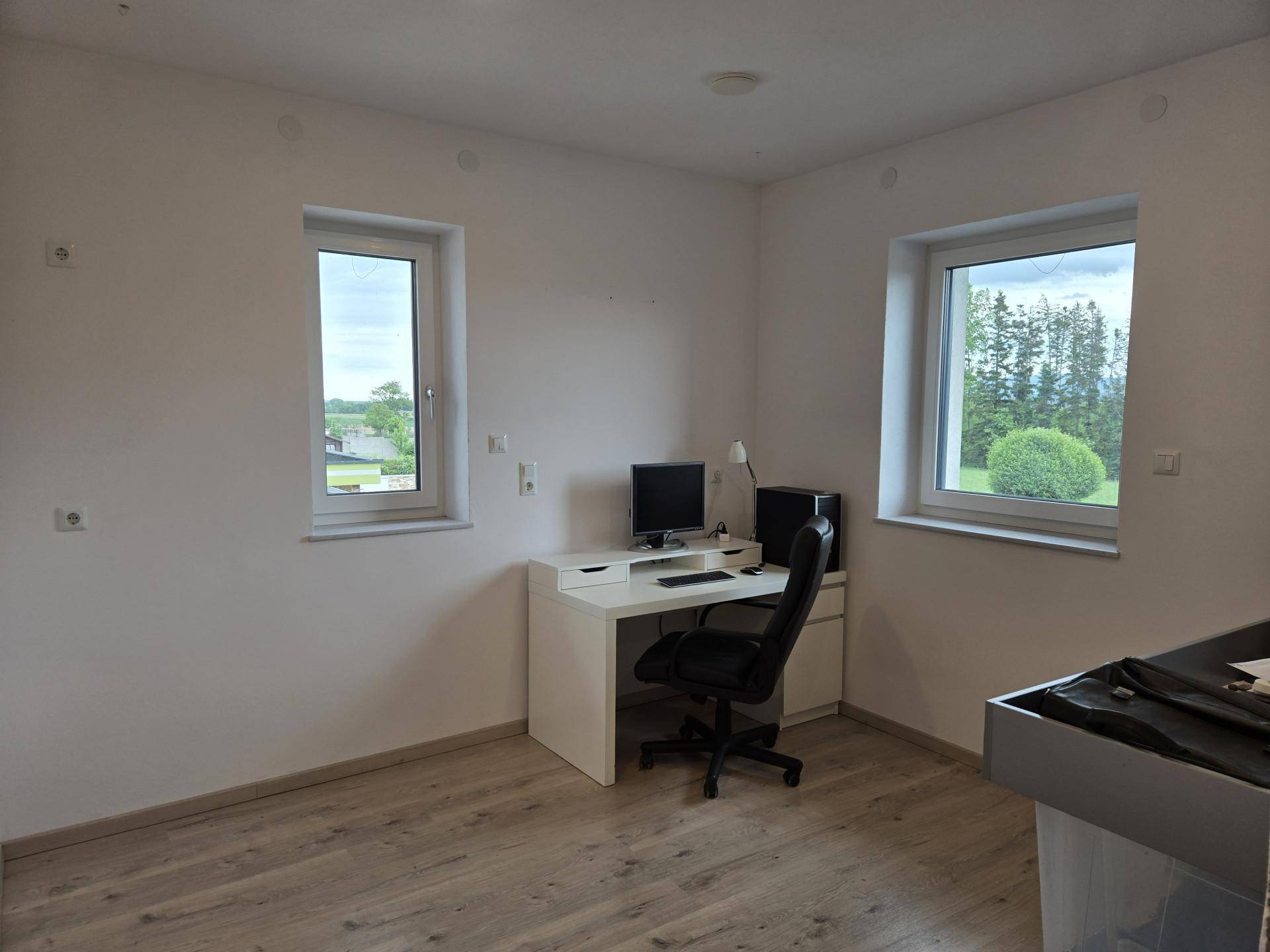 Helles Arbeitszimmer mit Schreibtisch, Bürostuhl und zwei Fenstern mit Blick ins Grüne.
