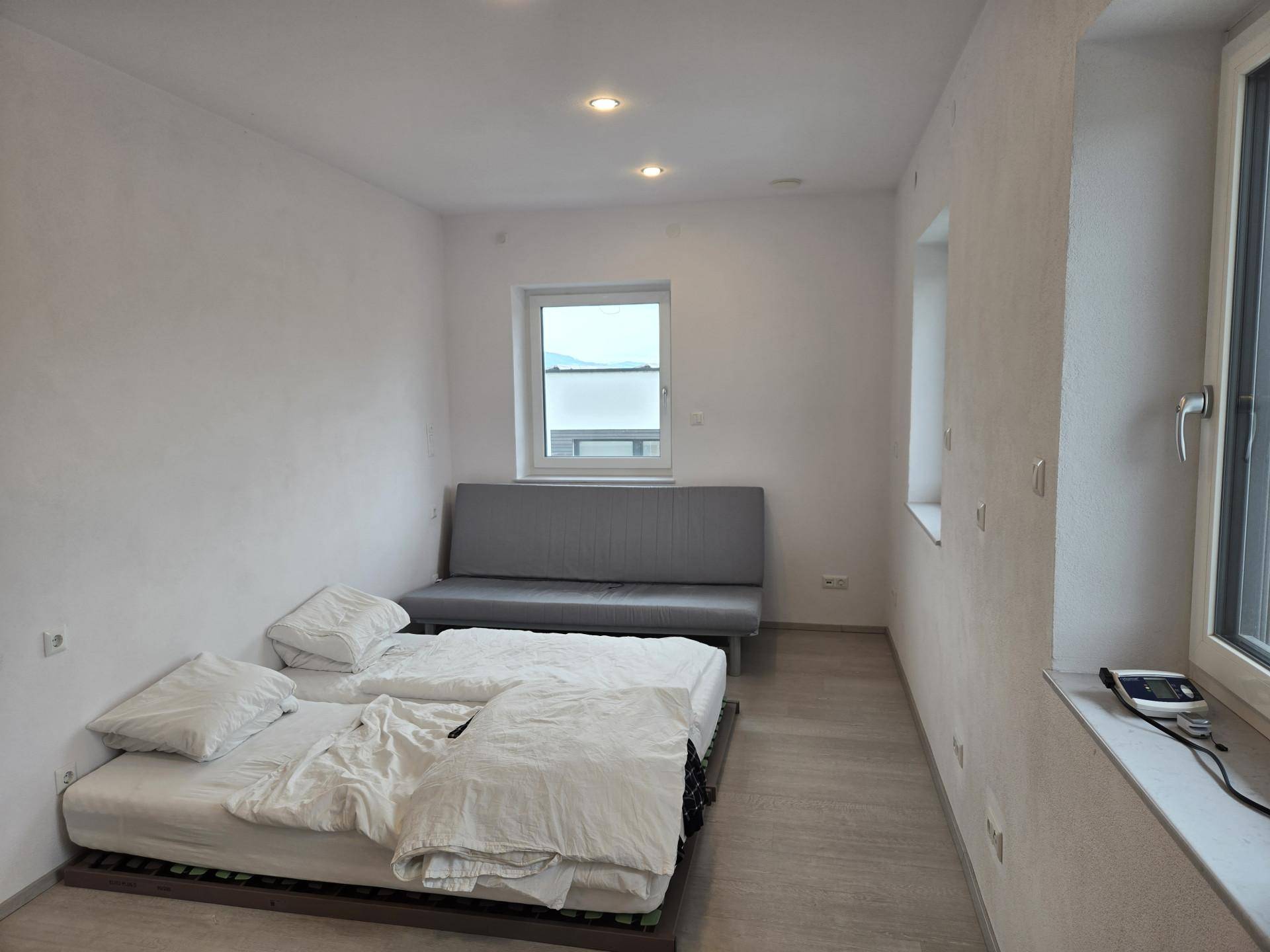 Schlichtes Schlafzimmer mit zwei Betten, einem Sofa und hellen Wänden, ideal für Gäste.