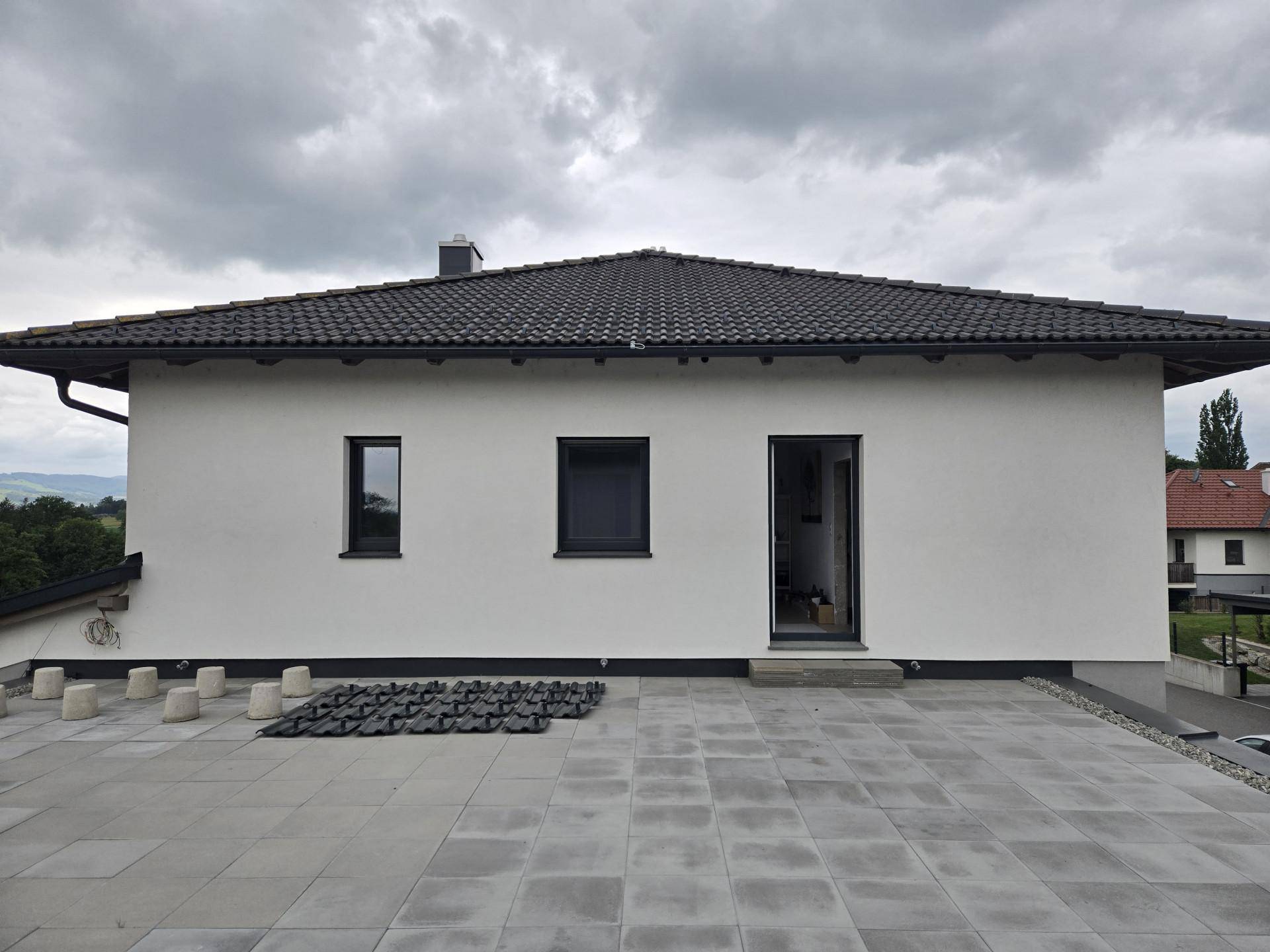 Große gepflasterte Terrasse an der Hausseite mit Zugang zum Garten und Blick auf die Umgebung.