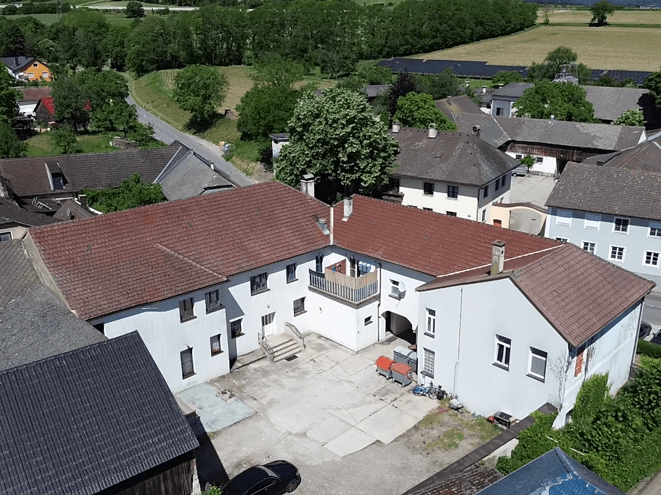 Luftaufnahme eines U-förmigen Gebäudekomplexes mit Innenhof und roten Ziegeldächern in ländlicher Umgebung.