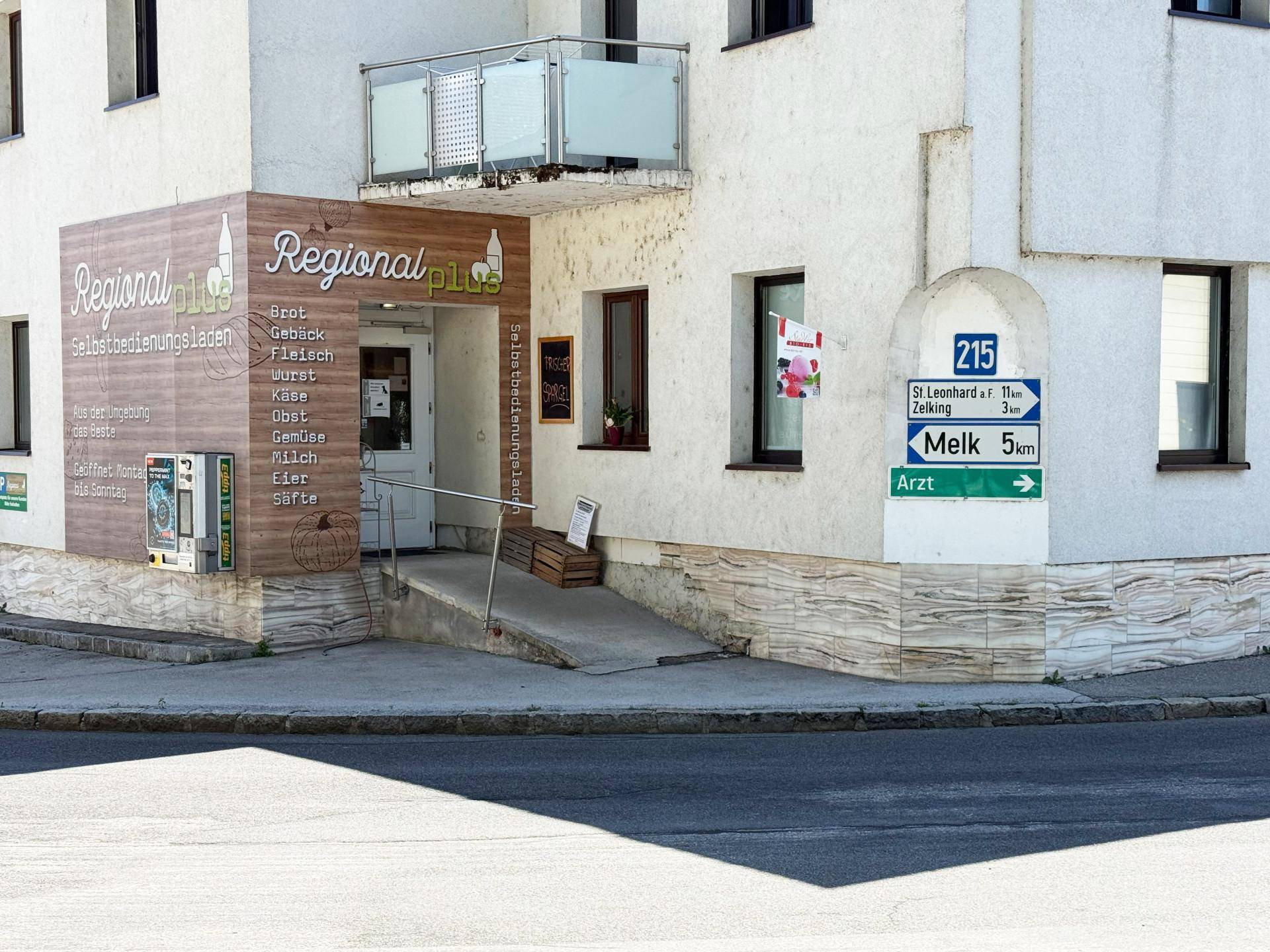Nahaufnahme des Eingangs eines Geschäfts mit Rampe, Beschilderung und einem kleinen Balkon darüber.
