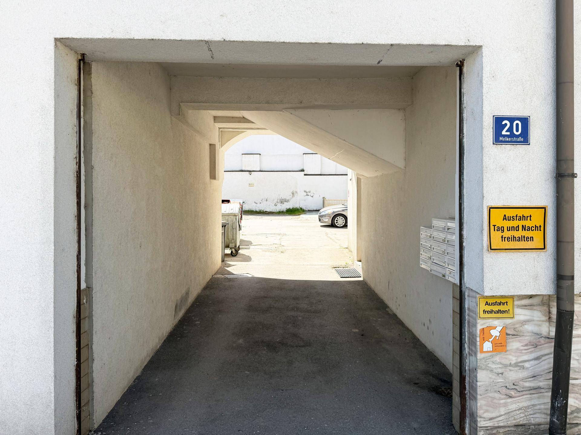 Überdachter Durchgang zu einem Hinterhof mit Parkplätzen und einem Briefkasten an der Wand.