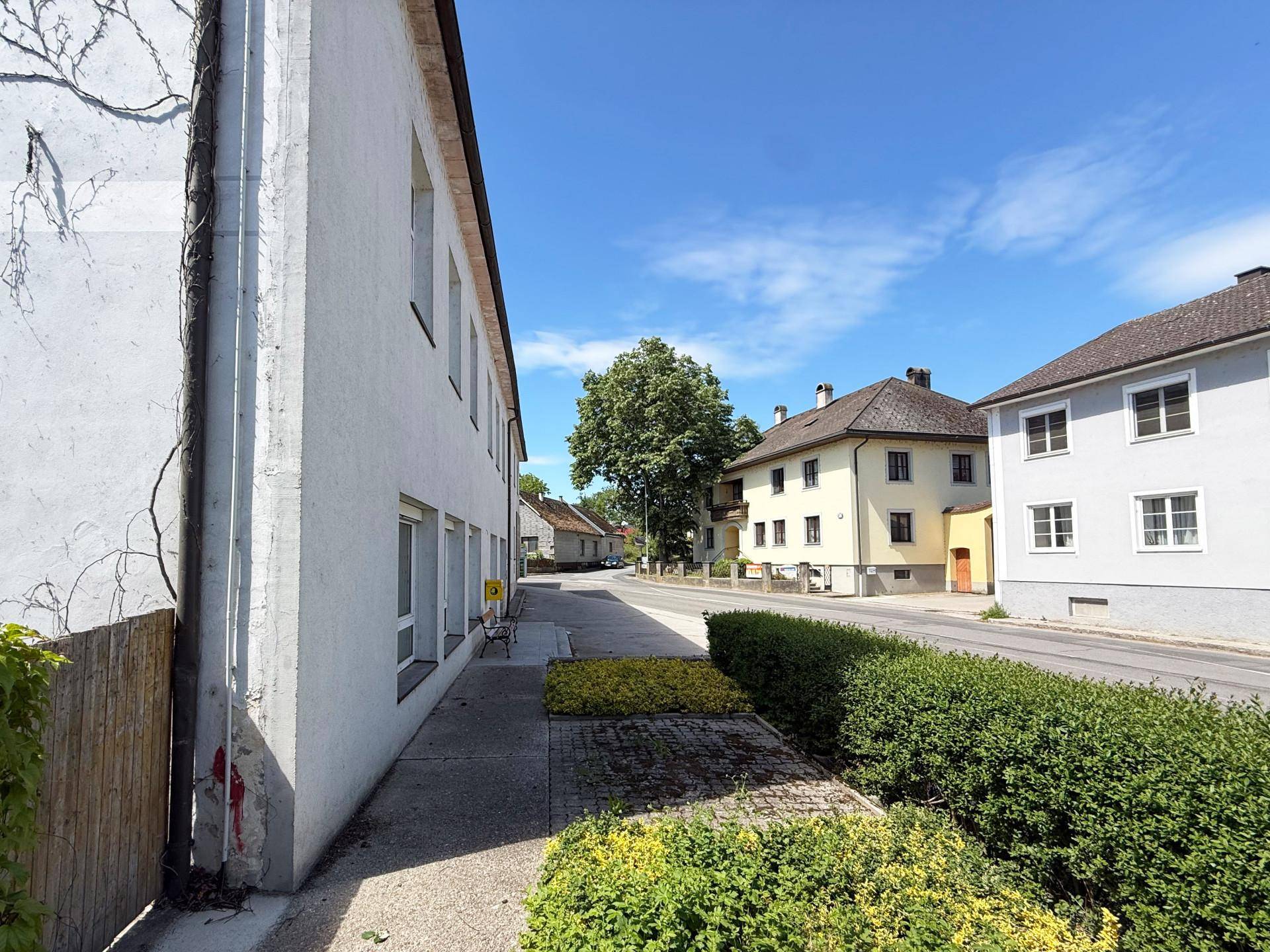 Seitenansicht eines weißen Gebäudes mit Fenstern, einer Hecke und einer ruhigen Straße daneben.