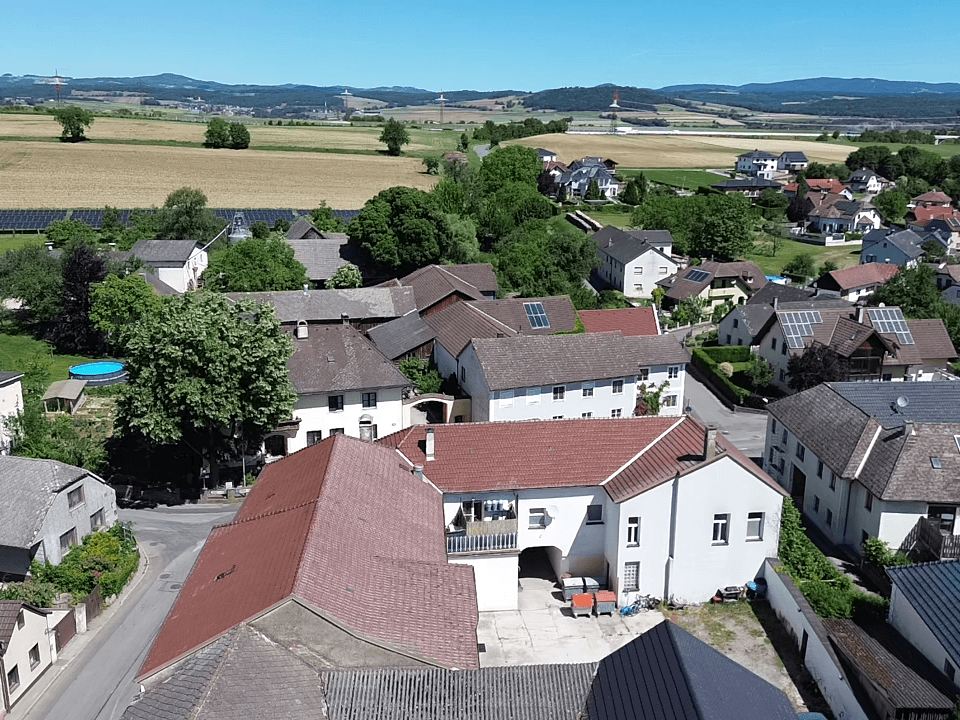 Weitläufige Luftaufnahme eines Dorfes mit Feldern, Wäldern und Solaranlagen in der Ferne.