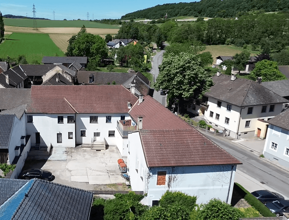 Luftaufnahme eines Gebäudekomplexes mit Innenhof, roten Ziegeldächern und einer Straße in ländlicher Umgebung.