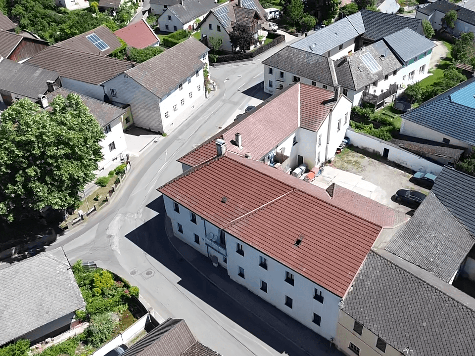 Luftaufnahme eines Gebäudekomplexes mit roten Ziegeldächern, Parkplätzen und einer Straße in einem Dorf.
