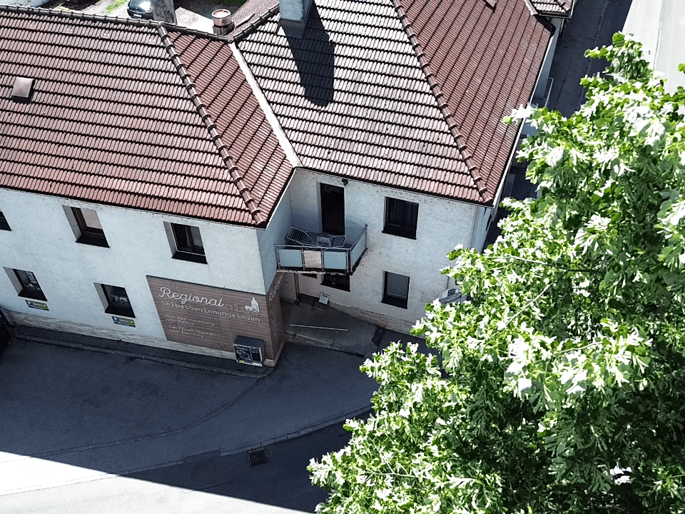 Nahaufnahme aus der Luft eines Gebäudeecks mit rotem Ziegeldach, Balkon und Geschäftsbeschilderung.