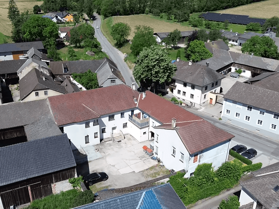 Luftaufnahme eines U-förmigen Gebäudekomplexes mit Innenhof, roten Ziegeldächern und einer Straße.