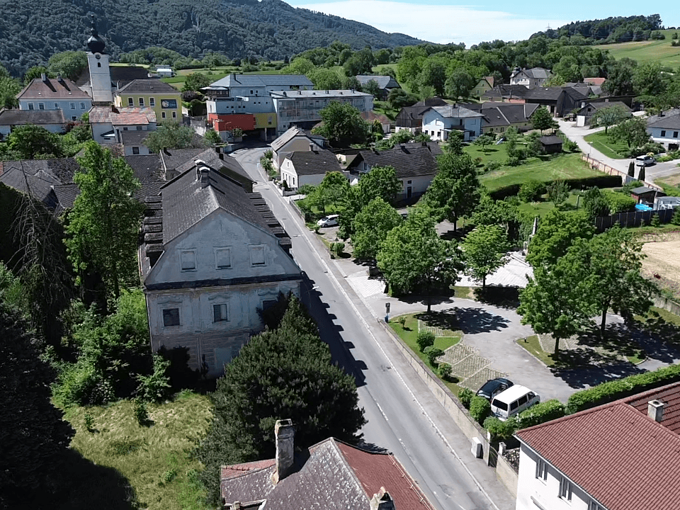 Weitläufige Luftaufnahme eines Dorfes mit einer Kirche, Häusern und grünen Hügeln im Hintergrund.