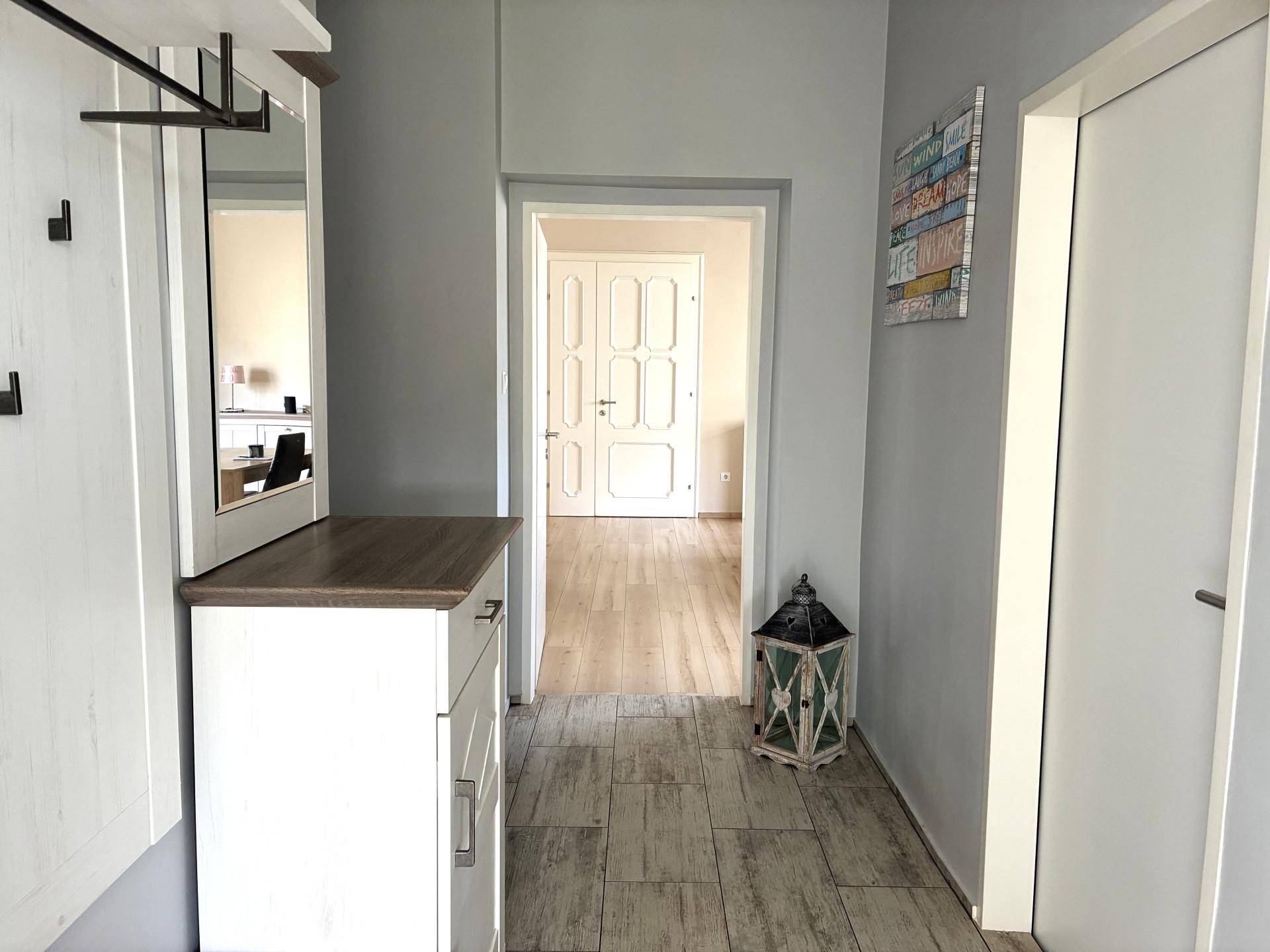 Flur mit Holzoptik-Fliesenboden, Garderobe und Blick in angrenzende Räume.